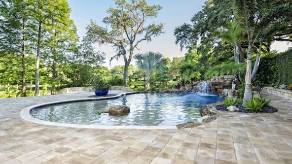 A beautiful landscaped swimming pool with waterfall at an estate home overlooking a lake in Florida.